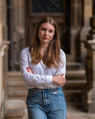 Close up portrait of a beautiful young Caucasian woman, cute girl on a city street, looking at the camera outdoors. She folded her hands on her chest. Lifestyle, female beauty concept. © Alexander