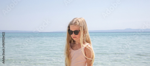 Portrait of 7 years old girl in pink swimsuit and long blonde hair with blue sea and sky in the background photo