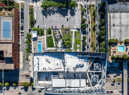 Aerial top view of a skyscraper with roof top area including air-conditioning, other equipment and recreational area including swimming pool and lawn area on floor level and surrounding buildings photo