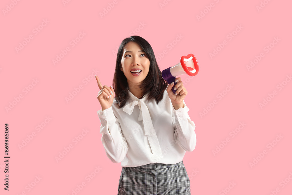 Naklejka premium Beautiful Asian woman with funny megaphone pointing at something on pink background. Dialogue concept