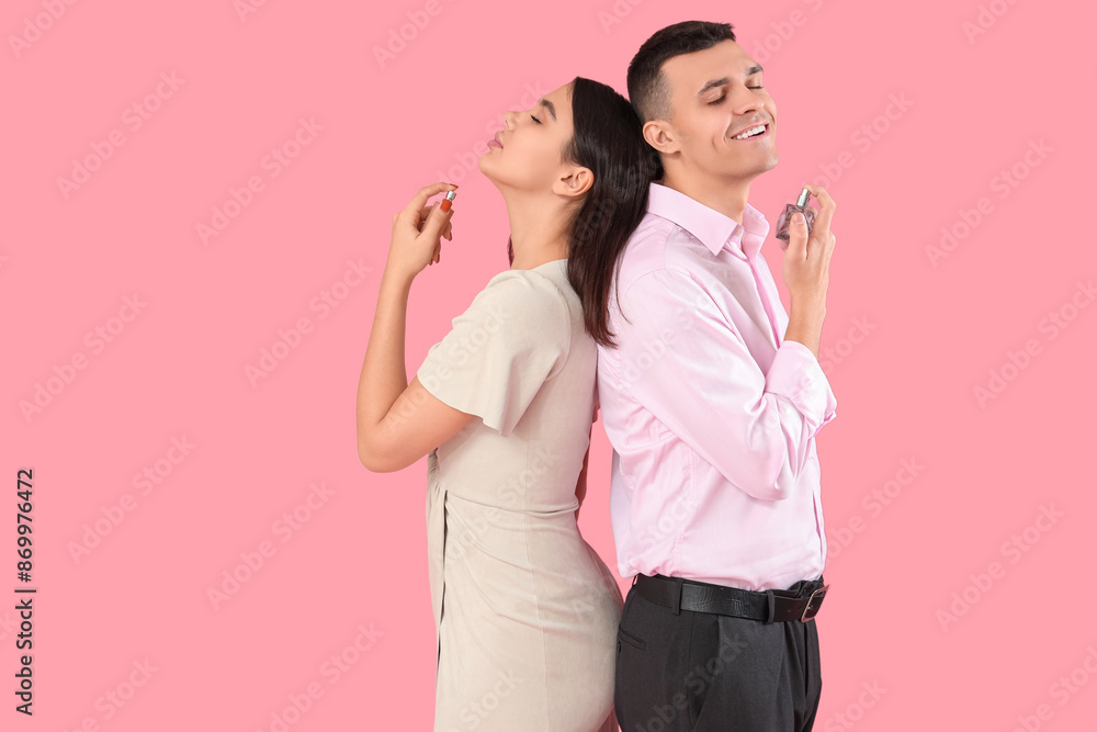 Young couple applying perfume on pink background Young couple applying perfume on pink background