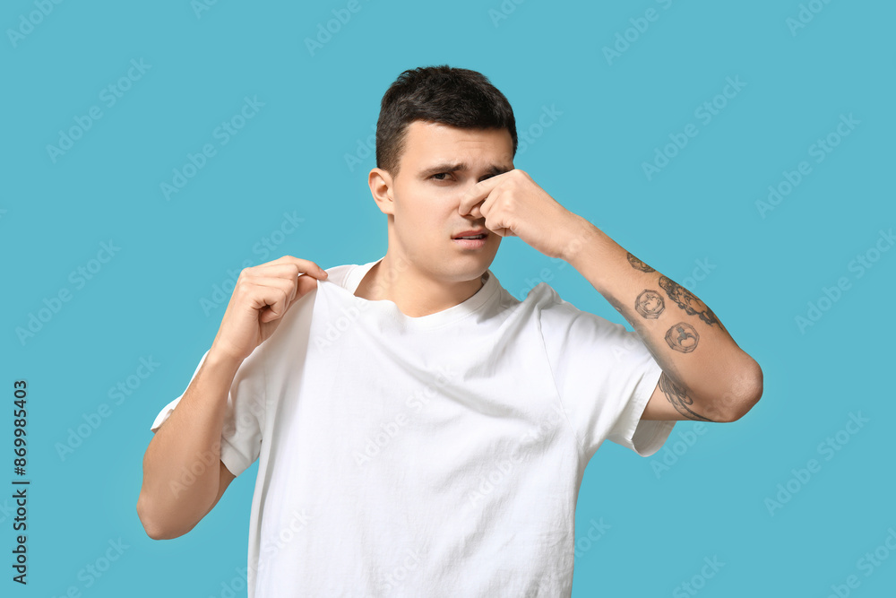 Fototapeta premium Handsome young man feeling bad smell from dirty clothes on blue background