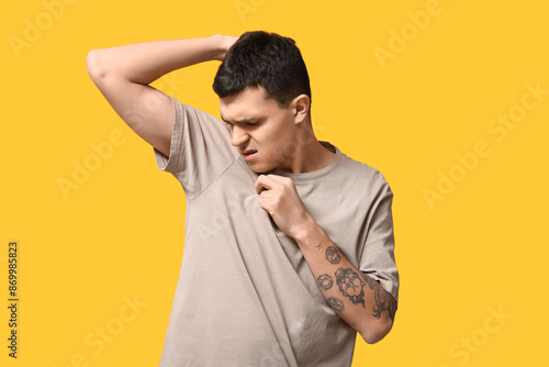Handsome young man feeling bad smell from armpits on yellow background photo