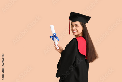 Happy female graduating student with diploma on beige background
