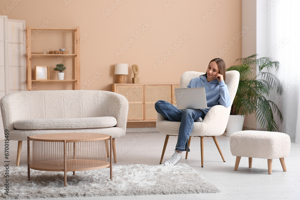Young woman sitting on armchair and using laptop in living room Young woman sitting on armchair and using laptop in living room