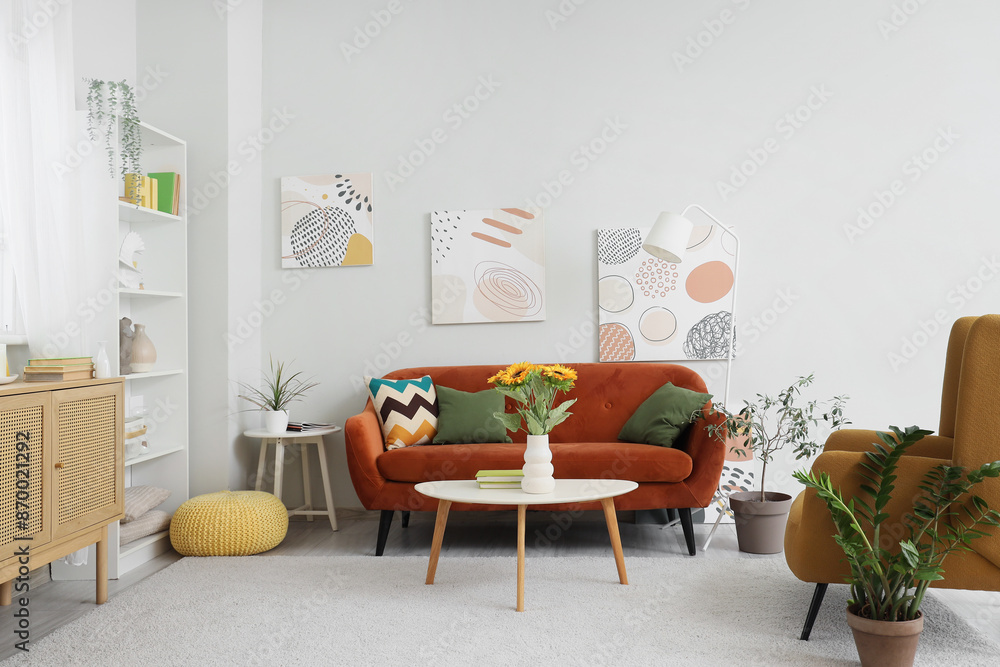 Fototapeta premium Comfortable sofa and sunflower in vase on table in living room