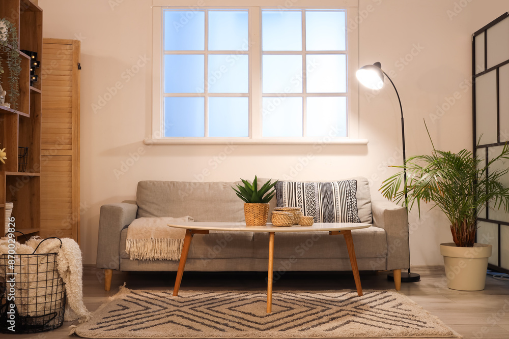 Fototapeta premium Interior of stylish living room with comfortable sofa, coffee table and glowing lamps