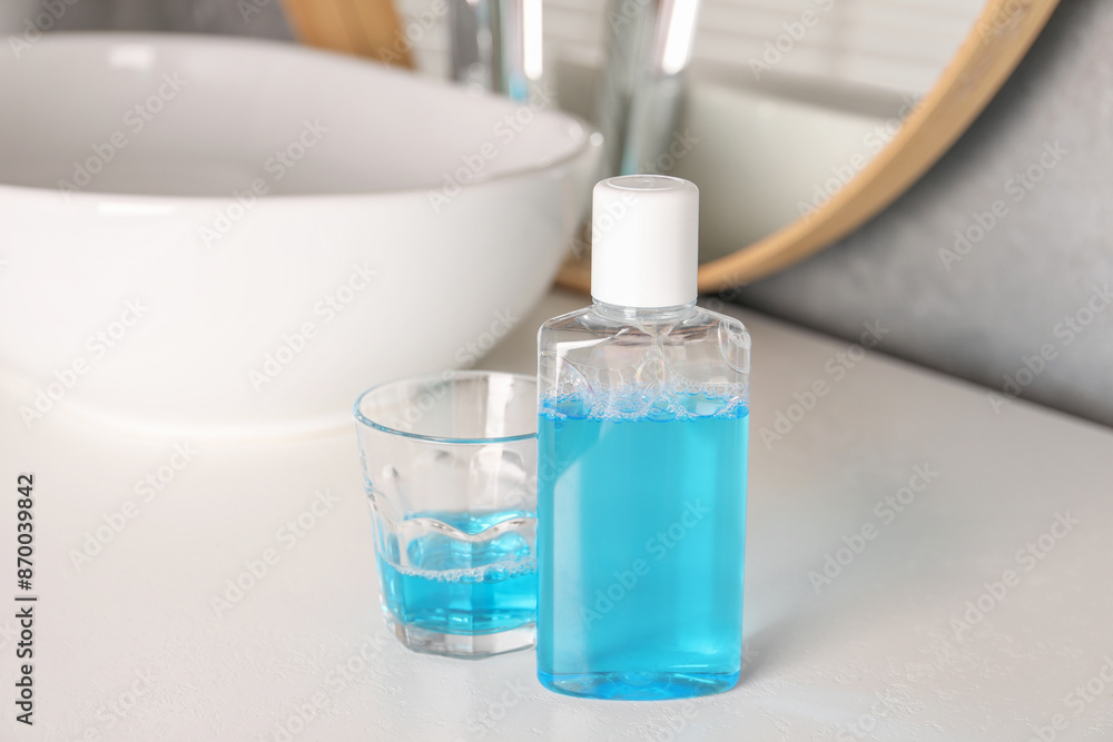 Bottle and glass of mouthwash on white countertop in bathroom Bottle and glass of mouthwash on white countertop in bathroom