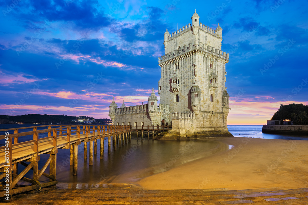 Fototapeta premium Belem Tower or Tower of St Vincent - famous tourist landmark of Lisboa and tourism attraction - on the bank of the Tagus River (Tejo) after sunset in dusk twilight with dramatic sky. Lisbon, Portugal