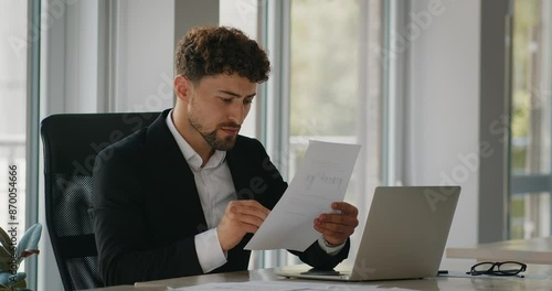 Serious financier checking documents, analyzing financial papers, preparing audit report at workplace.