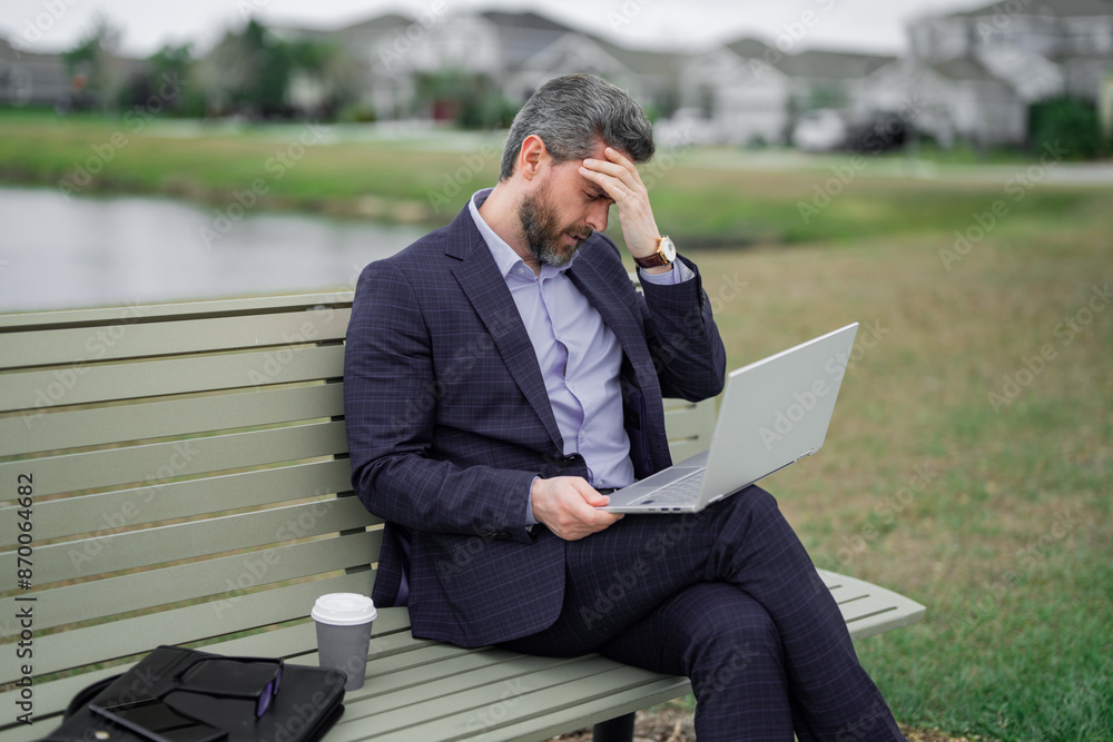 Stressed business man in suit sitting on bench. Stressed ceo manager work on laptop. Business man have stress and headache. Head pain migraine. Tired freelancer man online work from laptop in park. Stressed business man in suit sitting on bench. Stressed ceo manager work on laptop. Business man have stress and headache. Head pain migraine. Tired freelancer man online work from laptop in park.