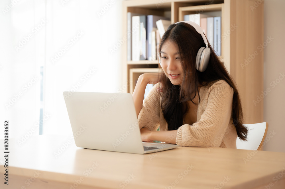 Young asian woman wearing headset while working on computer laptop at house. Work at home, Video conference, Video call, Student learning online class Young asian woman wearing headset while working on computer laptop at house. Work at home, Video conference, Video call, Student learning online class