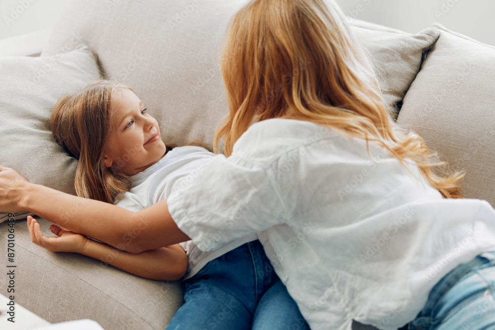 A mother and her daughter are bonding on the sofa at home, expressing affection and happiness A mother and her daughter are bonding on the sofa at home, expressing affection and happiness