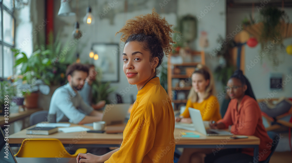 Obraz premium Young woman in a yellow sweater looks back while working in a vibrant, diverse coworking space.