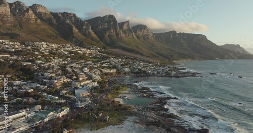 Drone flies over the camps bay in cape town south africa - many houses on a hillside - drone flies backwards over houses with view to table mountain and rocks in the sea