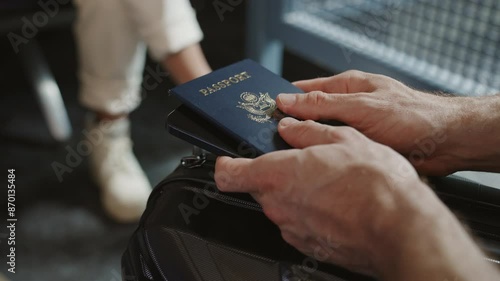 Close up on hands holding passport while waiting to board international flight in airport terminal or gate. Man taps fingers bored and impatient. Flight delay or cancellation. People sitting in lounge