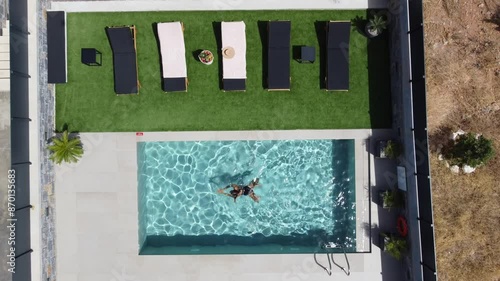 Drone flies over an outdoor pool in bird's eye view - Woman in swimming costume swims from one side to the other - Villa in Greece Crete with palm trees photo