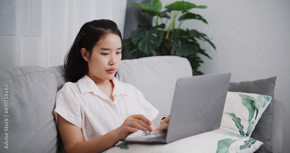 Portrait of Young asian woman using laptop on sofa in the living room at home ,Lifestyle with device technology, Working from home Portrait of Young asian woman using laptop on sofa in the living room at home ,Lifestyle with device technology, Working from home