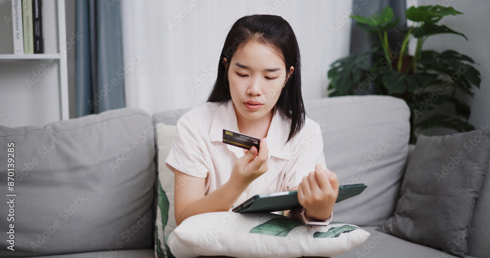 Portrait of Happy young woman sitting on sofa using credit card to pay on digital tablet in the living room at home ,Buy things online by tablet, Pay online. Portrait of Happy young woman sitting on sofa using credit card to pay on digital tablet in the living room at home ,Buy things online by tablet, Pay online.