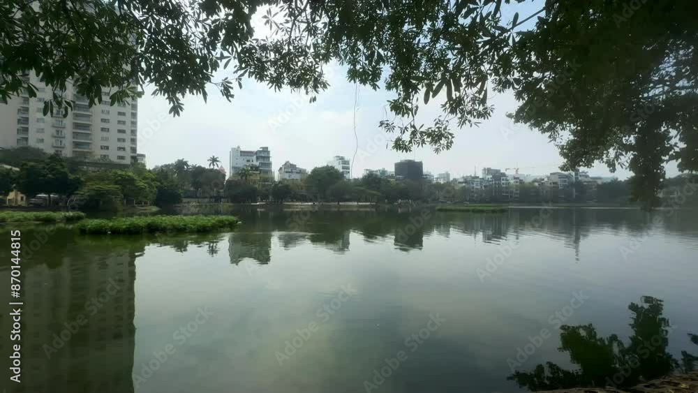 Panoramic view of a large lake with urban apartment buildings in the background. Asian inner city living. City lake with buildings, water, trees and bushes. True Bach lake. Ha Noi, Vietnam. Panoramic view of a large lake with urban apartment buildings in the background. Asian inner city living. City lake with buildings, water, trees and bushes. True Bach lake. Ha Noi, Vietnam.