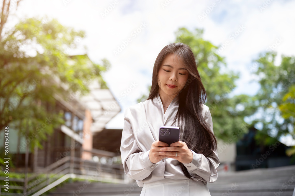 A positive Asian businesswoman is replying chat on her phone while walking down the stairs outdoors. A positive Asian businesswoman is replying chat on her phone while walking down the stairs outdoors.