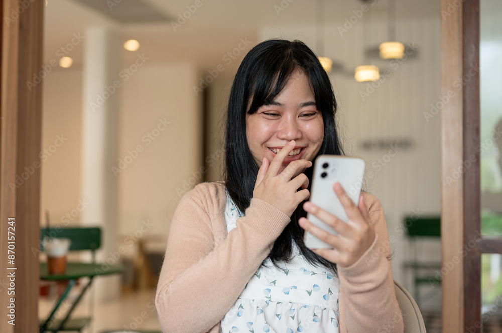 A cheerful Asian woman is laughing while reading messages on her smartphone. A cheerful Asian woman is laughing while reading messages on her smartphone.