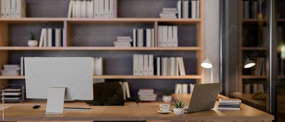 A contemporary luxurious private office at night features a computer and a laptop on a table. A contemporary luxurious private office at night features a computer and a laptop on a table.