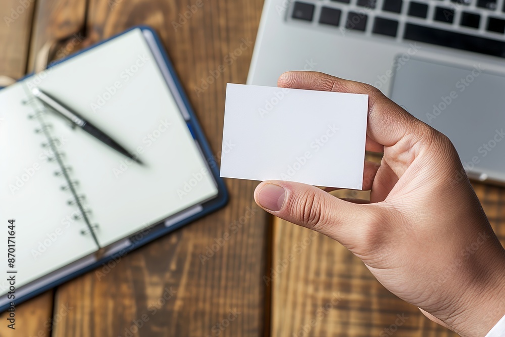 Hand Displaying Blank Business Card on Wooden Desk with Notepad and Laptop Hand Displaying Blank Business Card on Wooden Desk with Notepad and Laptop