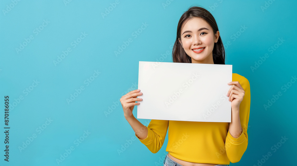Asian woman holding up a white sign, smiling at the camera against a solid blue background with a side view Asian woman holding up a white sign, smiling at the camera against a solid blue background with a side view