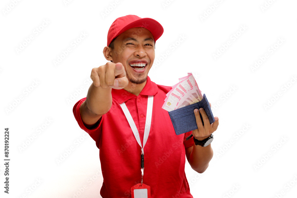 Asian delivery man or courier points towards the camera while holding money banknotes, isolated on white background. Concepts of professionalism, customer engagement, and secure monetary transactions. Asian delivery man or courier points towards the camera while holding money banknotes, isolated on white background. Concepts of professionalism, customer engagement, and secure monetary transactions.