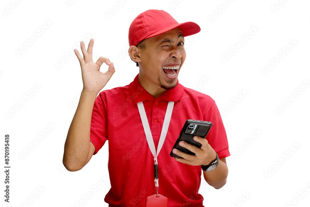 Asian delivery man or courier smiling and showing the OK gesture and winking to the camera while holding a phone. Isolated on a white background Asian delivery man or courier smiling and showing the OK gesture and winking to the camera while holding a phone. Isolated on a white background