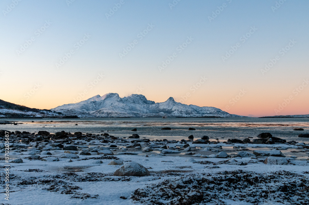 Landscape shot highlighting the rugged mountains and snow-covered beaches of arctic norway during a brief golden hour during the long winters. Landscape shot highlighting the rugged mountains and snow-covered beaches of arctic norway during a brief golden hour during the long winters.