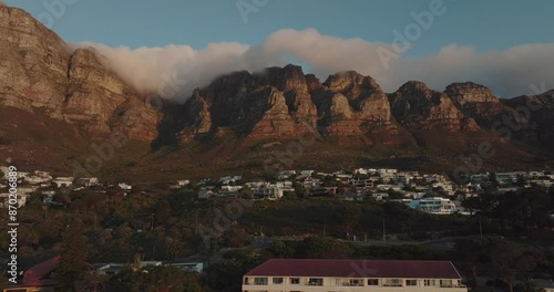 Drone flies slowly sideways over Camps Bay in Cape Town South Africa - Building on the hillside view of Table Mountain at sunset with light clouds