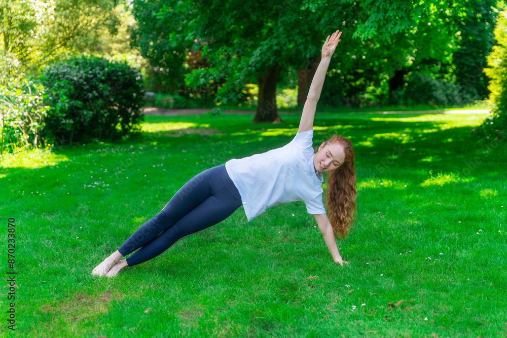 Fototapeta premium Woman Performing Side Plank Exercise On Grass In Park During Sunny Day