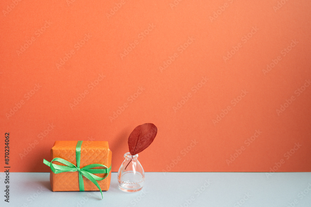 Orange gift box and vase of plant on gray desk. red wall background
