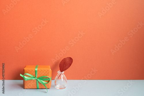 Obraz na płótnie Orange gift box and vase of plant on gray desk. red wall background w salonie