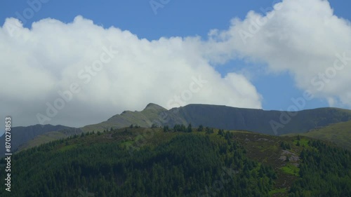 White clouds billowing rapidly over mountaintops fronted by pine forest during summer. Timelapse 60x. Ennerdale, English Lake District, Cumbria, UK photo