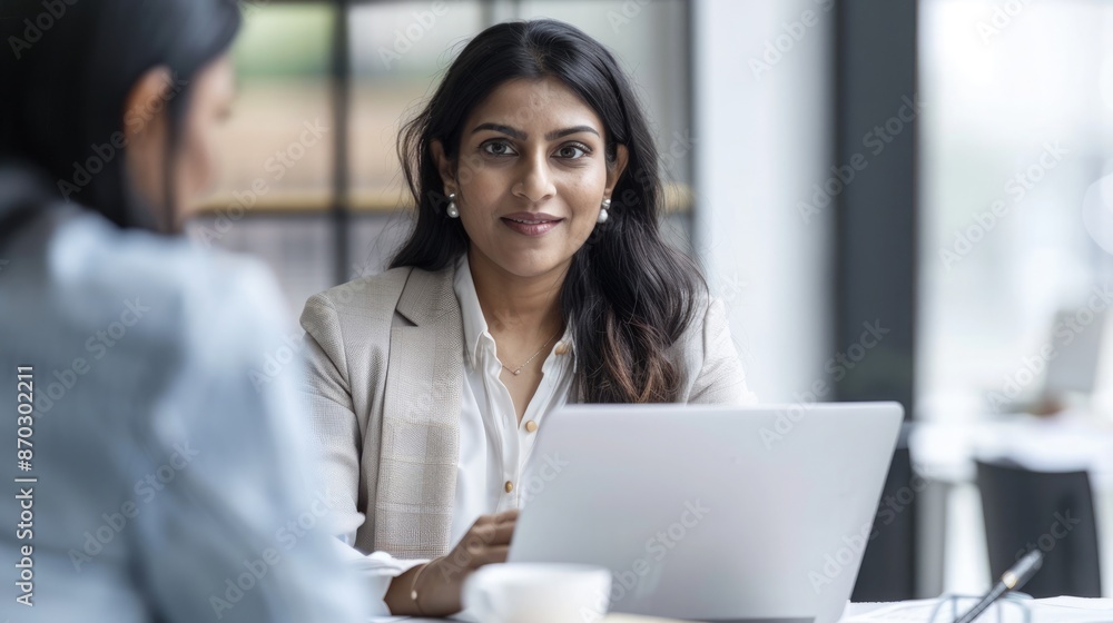 Indian mid-aged female manager using a laptop to finalize a deal, with client looking on in a professional setting. Mid aged manager successful deal Indian mid-aged female manager using a laptop to finalize a deal, with client looking on in a professional setting. Mid aged manager successful deal