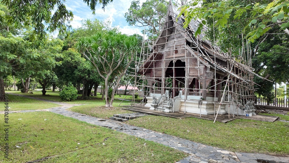 Traditional, old Thai pavilion, surrounded by scaffolding. Trees and bushes, a sign with Thai writing. Traditional, old Thai pavilion, surrounded by scaffolding. Trees and bushes, a sign with Thai writing.
