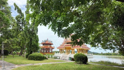 Park with trees, bushes and lawn. A lake, an Asian-style pavilion and hills.