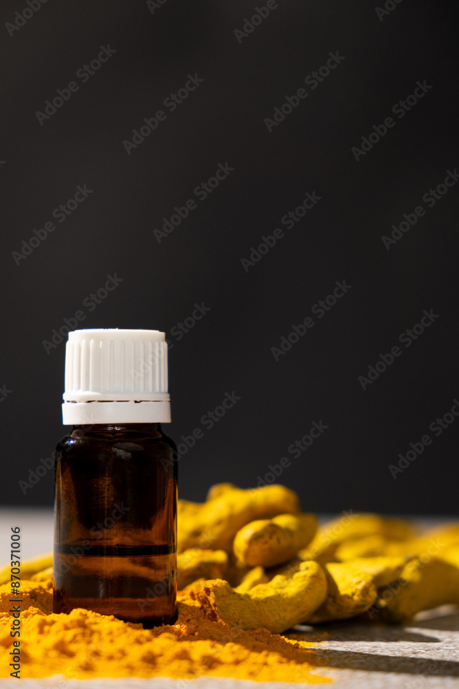 Turmeric essential oil in glass bottle among fresh turmeric and powder on black gray background. Turmeric essential oil in glass bottle among fresh turmeric and powder on black gray background.