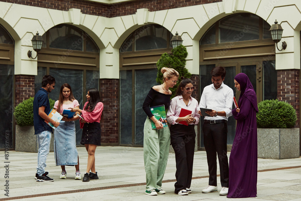 Fototapeta premium Group of students from different countries engaged in lively communication outdoors the university, studying, discussing personal and school life. Education, university, multicultural students concept