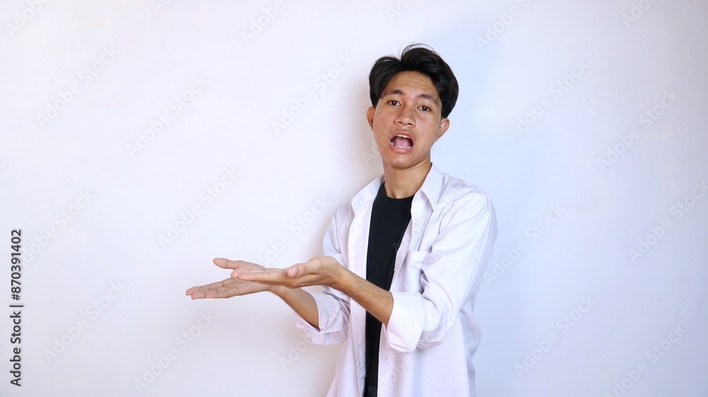 Excited young Asian man gesturing to the side using the palm of his hand Excited young Asian man gesturing to the side using the palm of his hand