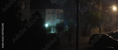 Heavy rain on the street in Eastern Europe. Night, lightning, one lantern is lit. Wet cars are parked next to the house.