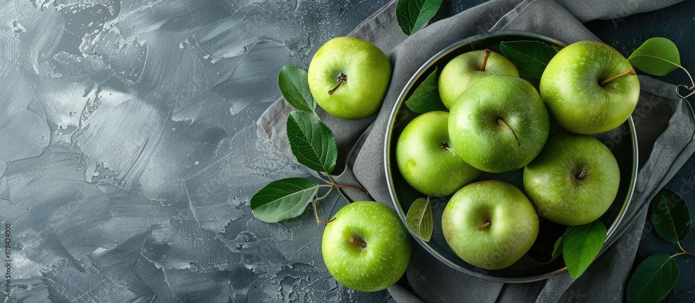 Green apples and leaves arranged in a metal bowl on a gray vintage napkin with wallpaper of fruits in a top-view flat lay composition, offering ample copy space image. Green apples and leaves arranged in a metal bowl on a gray vintage napkin with wallpaper of fruits in a top-view flat lay composition, offering ample copy space image.
