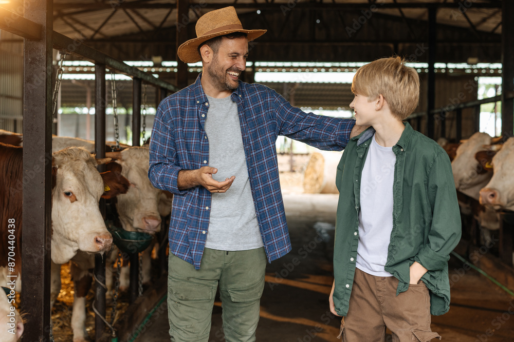 A boy and his farmer dad standing inside a cow barn A boy and his farmer dad standing inside a cow barn