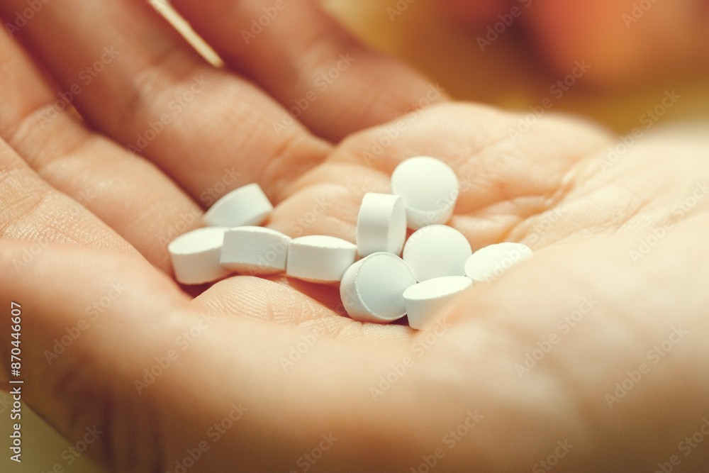 White round medical pills lie in hand, close up. These could be vitamins or antibiotics or pain relievers or any other. White round medical pills lie in hand, close up. These could be vitamins or antibiotics or pain relievers or any other.