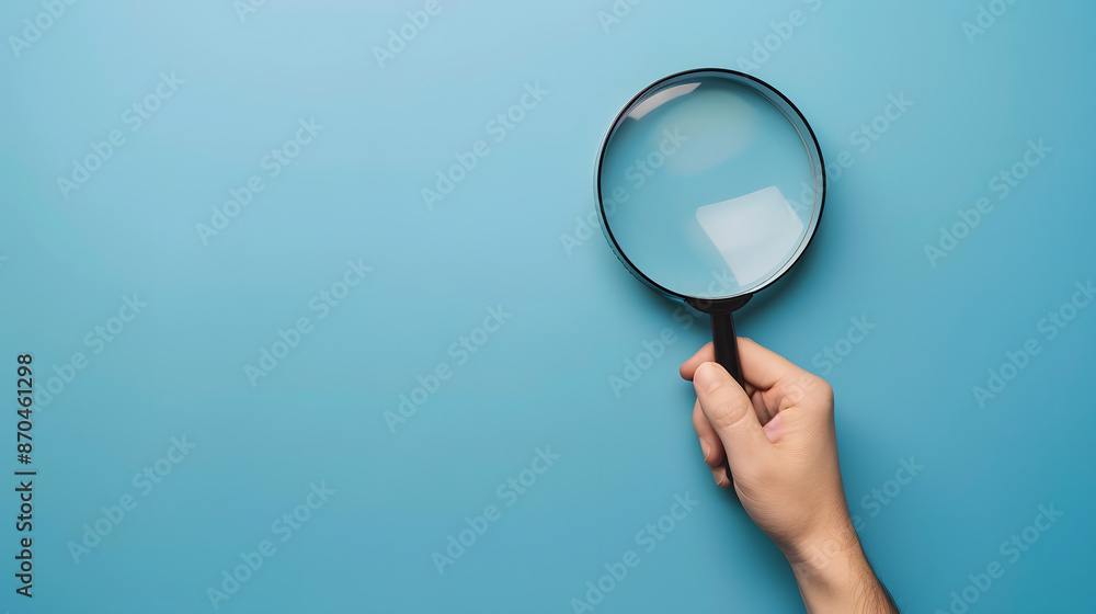 A close-up of a hand holding a magnifying glass against a blue background. The magnifying glass reflects light, symbolizing search, focus, and investigation concepts. A close-up of a hand holding a magnifying glass against a blue background. The magnifying glass reflects light, symbolizing search, focus, and investigation concepts.