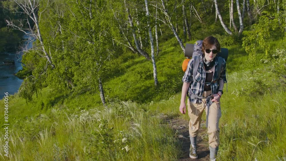 Tracking full shot of young Caucasian woman wearing comfortable casual clothes and sunglasses walking up hill and enjoying nature while hiking alone in summer Tracking full shot of young Caucasian woman wearing comfortable casual clothes and sunglasses walking up hill and enjoying nature while hiking alone in summer