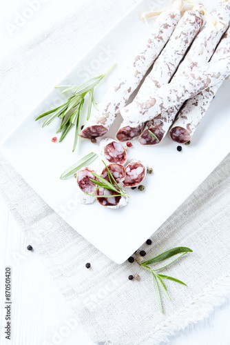 Foto Sliced french salami with fresh rosemary on white background